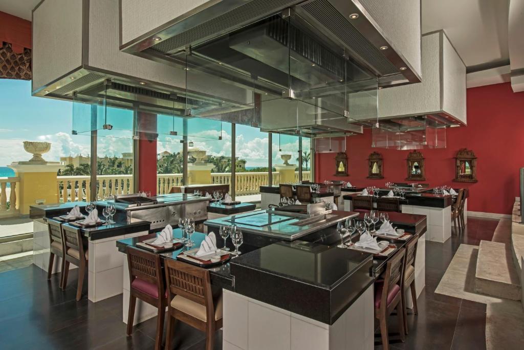 Mūsdienīgs restorāns ar panorāmas logiem un elegantiem galdiem, kas izrotāti ar stikla un melnu marmora virsmām. Aiz logiem redzams skaists skats uz dabu un jūru.