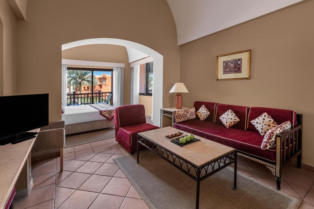 Jaz Makadi Saraya Resort numurs ar viesistabu un balkonu, redzama zaļa ainava.