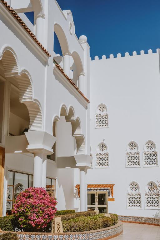 Baron Palms Resort baltā ēka ar arku un ziedu kompozīciju pie ieejas.