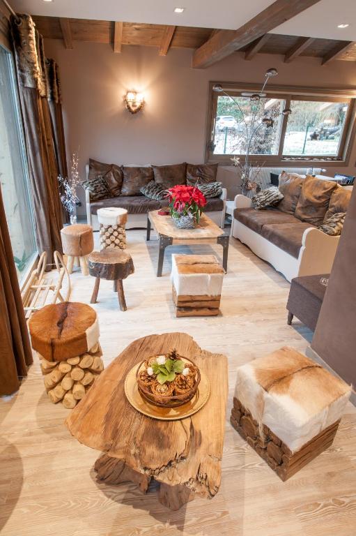 Mūsdienīgs viesistabas interjers ar koka mēbelēm un siltām krāsām, kurā redzama dīvāns, dažādas krēsli un galdi. Telpa ir dekorēta ar ziediem un dabīgiem elementiem, radot mājīgu atmosfēru.