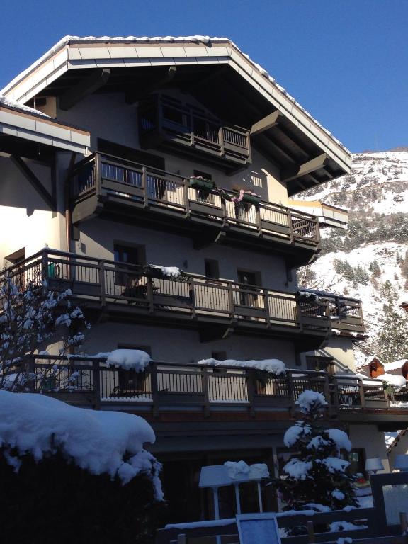 Kalnu viesnīca ar balkoniem, pārklātiem ar sniegu, un skatu uz kalniem. Zila debess un ziemas ainava papildina ēkas atmosfēru.