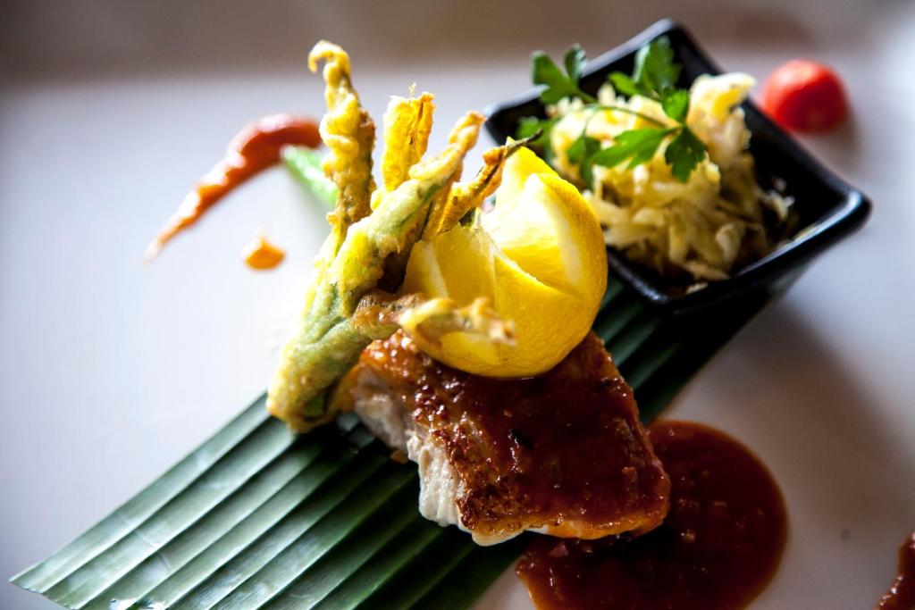 Garšīgs ēdiens ar ceptu zivi, dekorēts ar citronu un kraukšķīgu dārzeņu fritē. Blakus ir mērce un salāti.