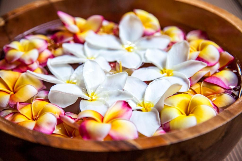 Ziedu kompozīcija ar baltiem un dzelteniem ziediem, kas peld koka traukā. Šī ainava rada mierīgu un relaksējošu atmosfēru.