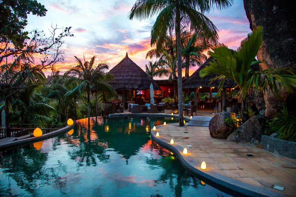 Tropu viesnīca ar peldbaseinu, apkārt palmām un romantisku saulrietu fona. Ap gaismas elementiem ap baseinu, kas rada mierīgu atmosfēru.