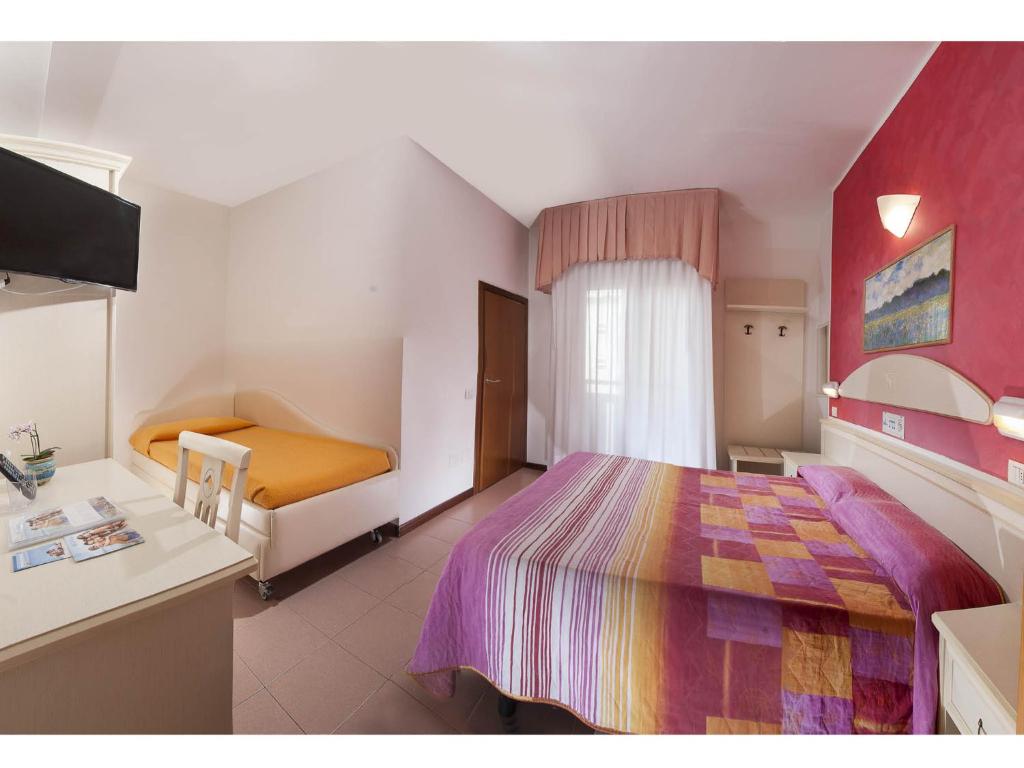 Mūsdienīgs viesnīcas numurs ar divām gultām, televizoru un interjera elementiem, kas veidoti siltās krāsās. Numurā ir arī galds un maza ziedu kompozīcija uz tā.