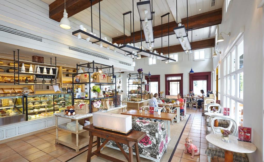 Mūsdienīgs kafejnīcas interjers ar gaišām krāsām, koka sijām un plašu vitrīnu, kas piedāvā dažādus konditorejas izstrādājumus un dzērienus. Apmeklētāji relaksējas pie galdiņiem un baudījuši atmosfēru.