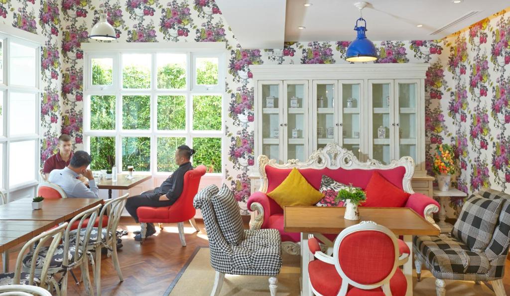 Kafijas telpa ar krāsainu ziedu tapeti, modernām mēbelēm un viesiem, kas sarunājas pie galda. Gaisīga atmosfēra un dabiskā apgaismojuma pieplūdums caur lielajiem logiem.