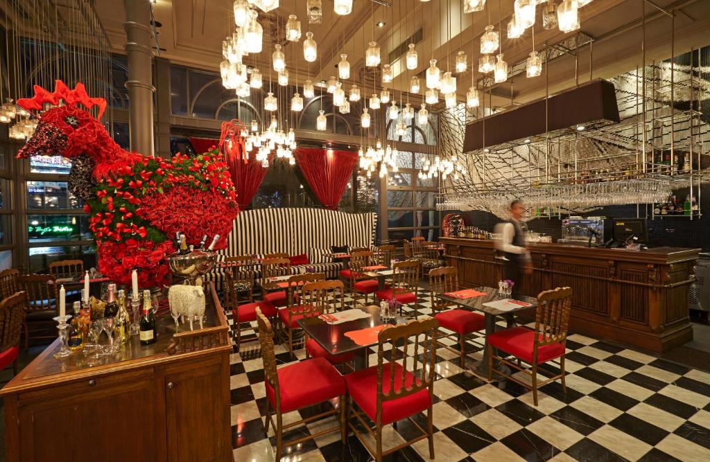 Restorāns ar elegantu interjeru, kurā ir izteikta ziedu kompozīcija, kas veidota kā vistas figūra, un moderns apgaismojums. Galdi ir ar sarkaniem krēsliem un melnbaltu grīdu.