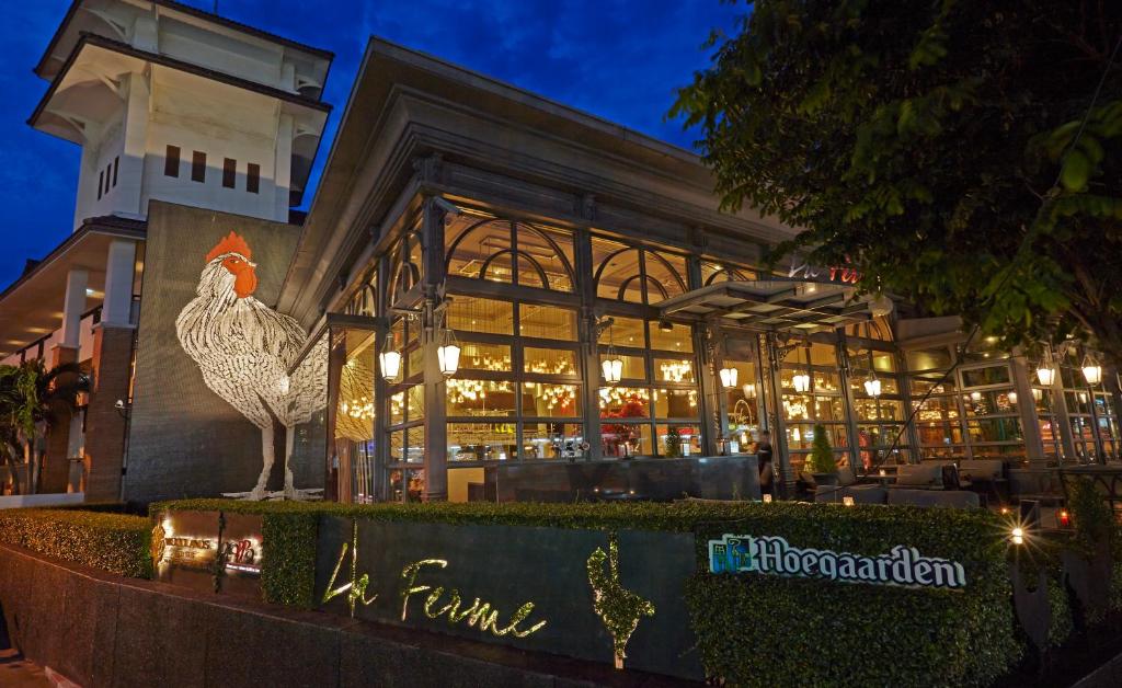 Restorāna "La Ferme" izskats ar lielu vistas attēlu un modernu arhitektūru, izceļoties vakarā. Apgaismojums un augu dekorācijas piešķir patīkamu atmosfēru.