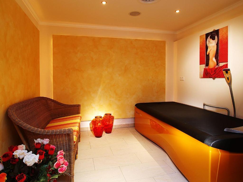 Relaksējoša spa telpa ar dzeltenām sienām, melnu gultu un vītnēm, kā arī ziedu kompozīciju. Telpā ir arī sarkani trauki un mākslas darbs uz sienas, kas piešķir viesmīlīgu atmosfēru.