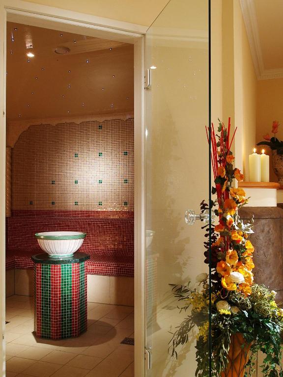 Eleganta pirts telpa ar mozaīkas sienām un dekoratīvām ziedu kompozīcijām, radot relaksējošu atmosfēru. Centrā atrodas krāsains baseins un sēdvietas.