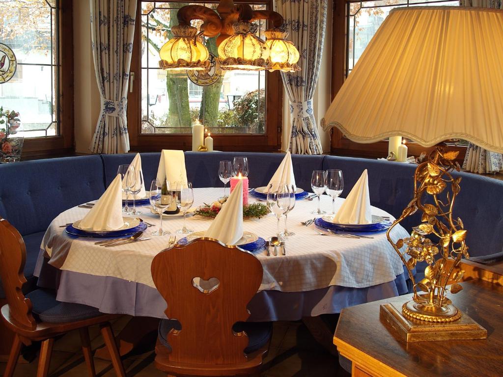 Elegants restorāna galdiņš ar zilu dīvānu, dekorēts ar baltām galdautām un izsmalcinātām viesību piederumiem. Gaismas spuldzes un sveces piešķir mājīgu atmosfēru.