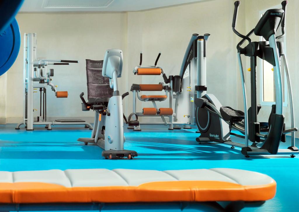Mūsdienīgs sporta zāles interjers ar dažādām trenažieriem un vingrošanas aprīkojumu uz gaiši zila grīdas.
