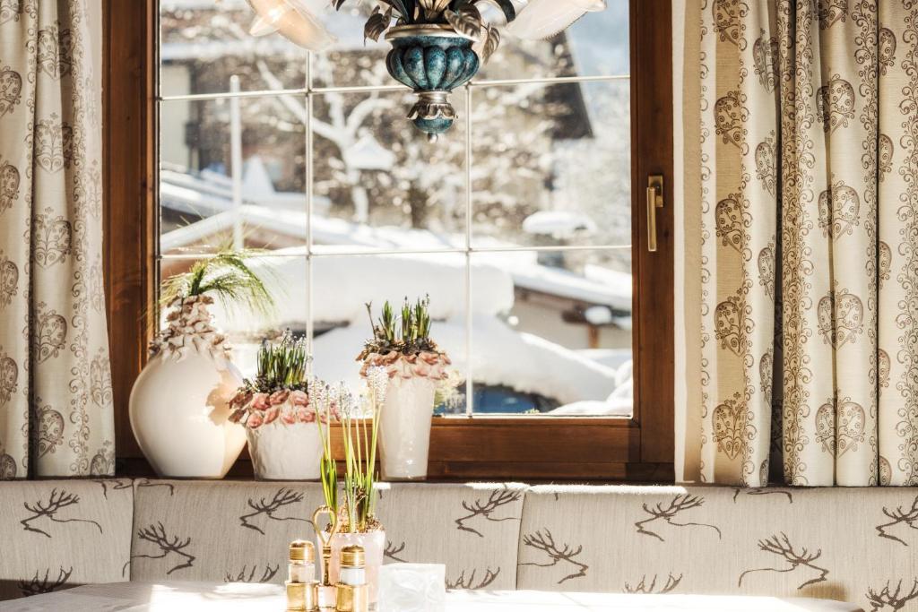 Gaismas piepildīta interjers ar logu, caur kuru redzama ziemas ainava. Uz palodzes izvietoti dekoratīvi puķu podi un elegants apgaismojums.