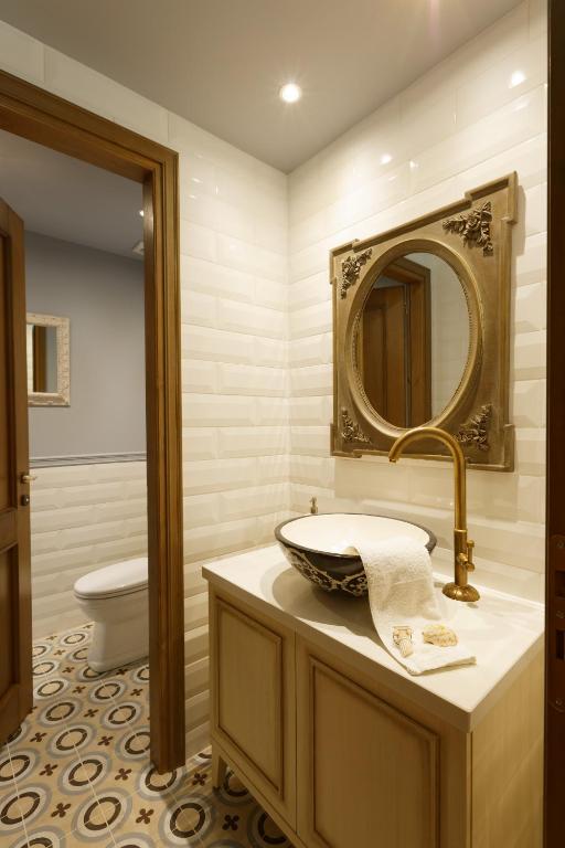 Mūsdienīgs vannas istabas interjers ar elegantu izlietni un dekoratīvu spoguli, apvienojot pelēkas un baltas flīzes ar krāsainu grīdu.