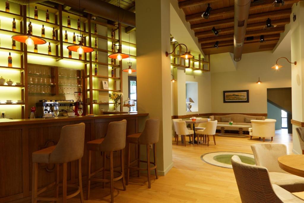 Mūsdienīgs bārs ar koka interjeru un stilīgām lampām, aiz kura redzami plaukti ar dzērienu pudelēm. Viegli iekārtotas sēdvietas un silta atmosfēra.