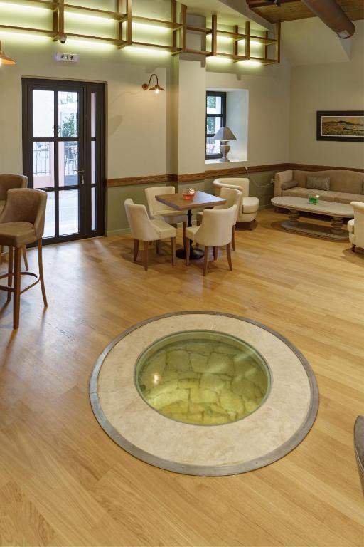 Interjera skats ar elegantiem krēsliem un galdiņiem, kā arī apaļu ūdens elementu grīdā. Gaisma ieplūst caur logiem, radot patīkamu atmosfēru.