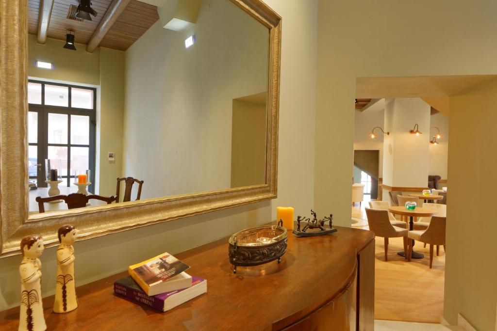 Interjera attēls ar elegantu spoguli un ornamentālu mēbeļu kompozīciju, kas rada viesmīlīgu atmosfēru. Redzamas grāmatas un dekoratīvi priekšmeti uz galda, kā arī gaiši apgaismota telpa.