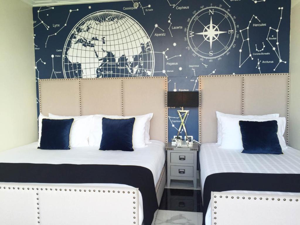 Moderna guļamistaba ar diviem gultām, zilu un baltu interjeru, un sienu, kurā attēlota pasaule un zvaigznāji. Ideāla telpa atpūtai un relaksācijai.