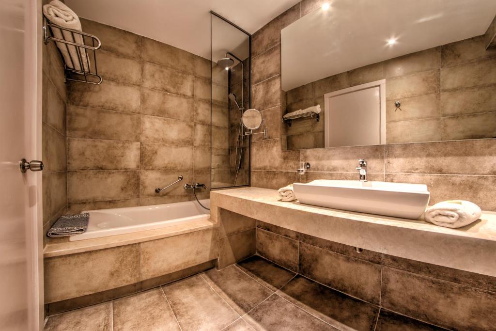 Mūsdienīgs vannas istabas interjers ar vannu, izlietni un flīzēm neitrālās krāsās, radot elegantu un relaksējošu atmosfēru.