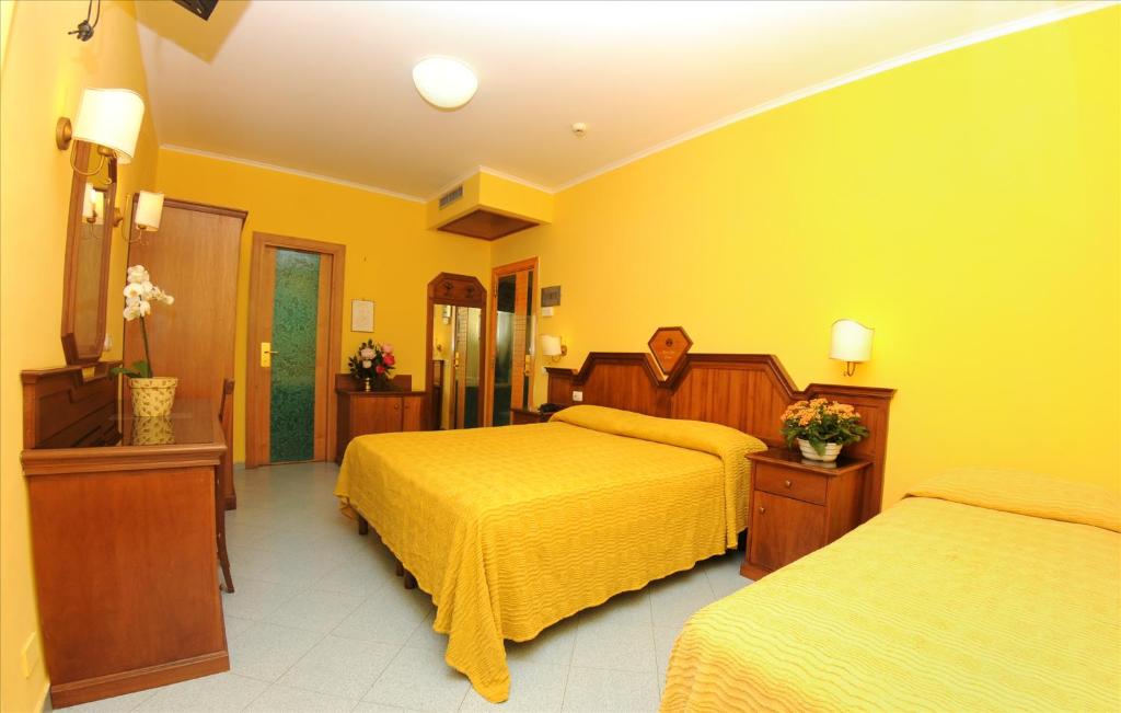 Dzeltenā viesnīcas numuriņa interjers ar divām gultām un koka mēbelēm, kas rada siltu un viesmīlīgu atmosfēru. Numuriņā ir arī spogulis un ziedi, kas piešķir patīkamu akcentu.