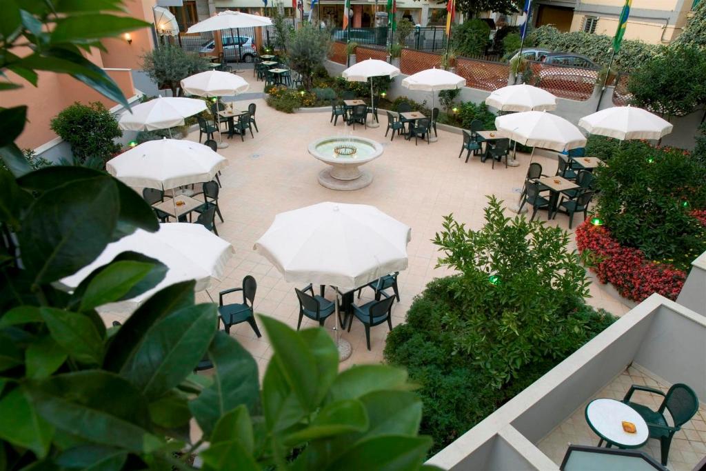 Mierīgā kafejnīca ar saulessargiem un zaļajiem augiem, kas veido patīkamu āra vidi. Centrā ir strūklaka, kas piešķir papildus šarmu.