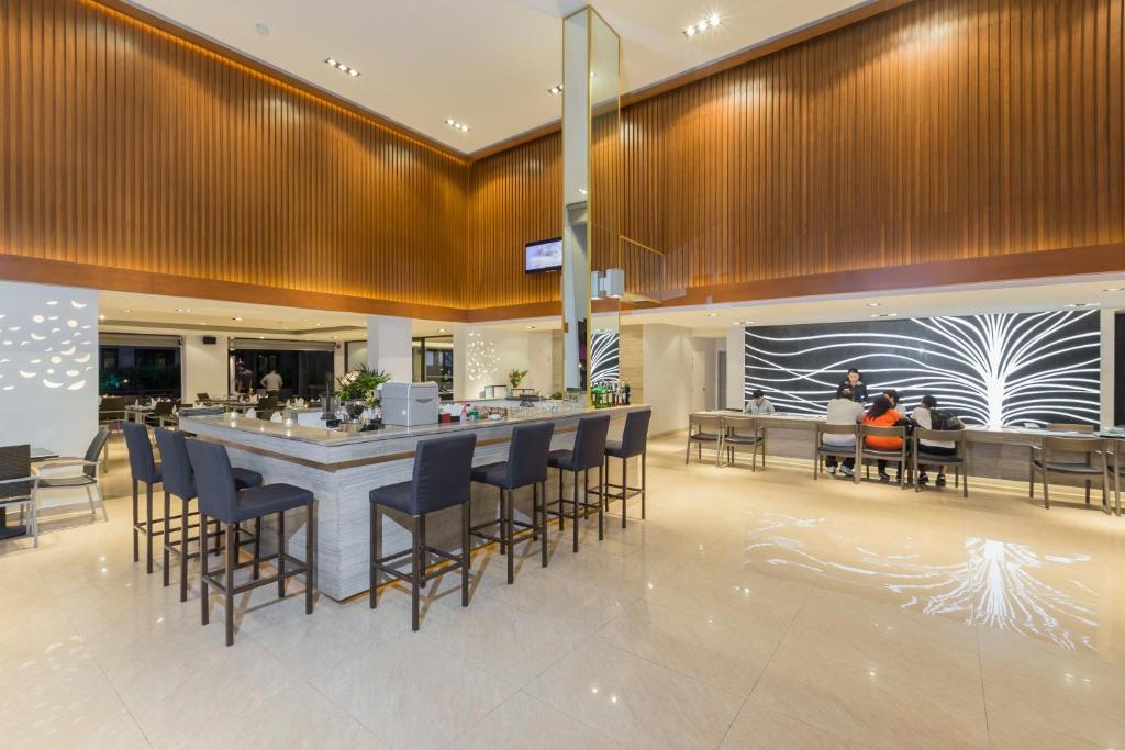 Mūsdienīgs bārs ar elegantu interjeru, kurā ir gaiši koka akcenti un stilīgs apgaismojums. Apmeklētāji sēž pie bāra un pie galdiem, baudot dzērienus un ēdienus.