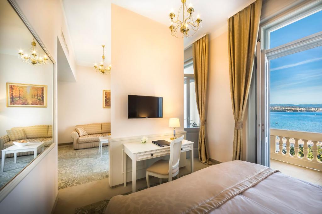 Mūsdienīgs viesnīcas numurs ar skatu uz jūru, kas iekārtots ar elegantu mēbelējumu un gaismas avotiem. Telpa ietver gultu, rakstāmgaldu un viesistabu ar dīvānu.