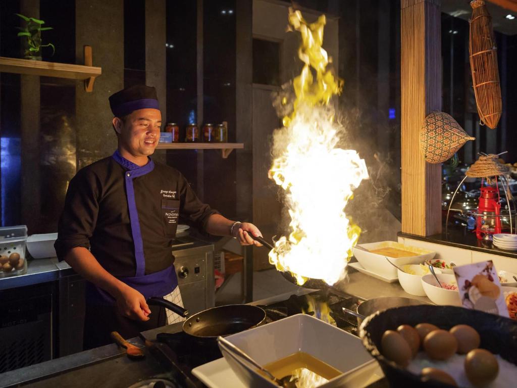 Pavārs gatavo liesmojošu ēdienu Novotel Phuket Kamala Beach virtuvē.