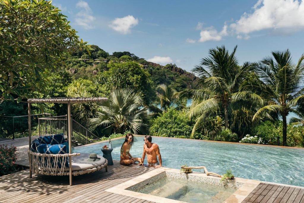 Pāris atpūšas privātā baseinā uz terases Four Seasons Resort Seychelles, ko ieskauj tropu zaļumi.