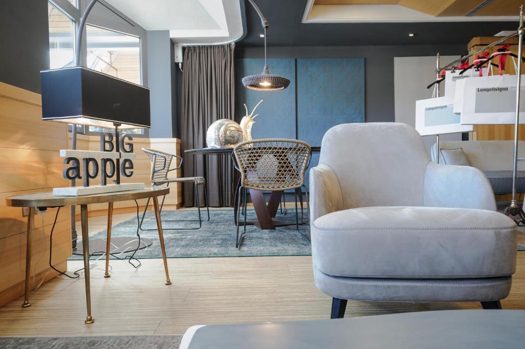 Moderns interjers ar ērtu pelēku krēslu un stilīgu galdu, uz kura redzams uzraksts "BIG apple". Telpā ir eleganta apgaismojuma un dekoratīvo elementu kombinācija, radot mājīgu atmosfēru.