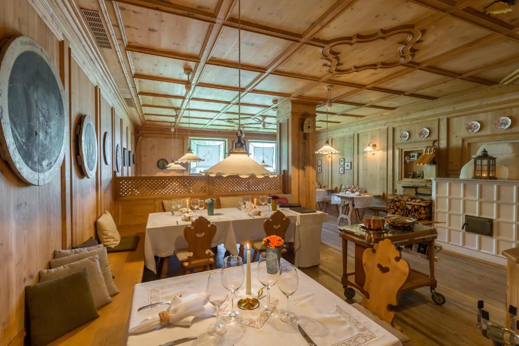 Eleganta restorāna iekārtojums ar koka sienām un galdiem, kas dekorēti ar ziediem un glāzēm. Gaisma ir silta un mājīga, radot patīkamu atmosfēru.