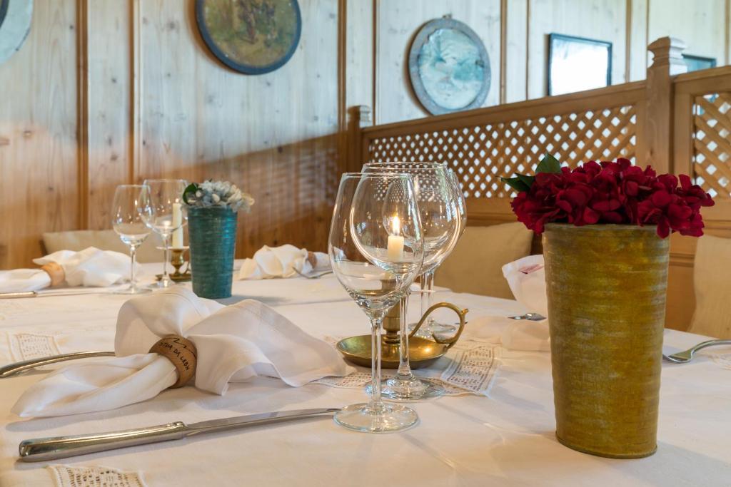 Eleganta galda noformējums ar ziediem un vīna glāzēm, radot patīkamu atmosfēru. Uz galda ir svece un sudraba galda piederumi, kas papildina romantisko noskaņu.