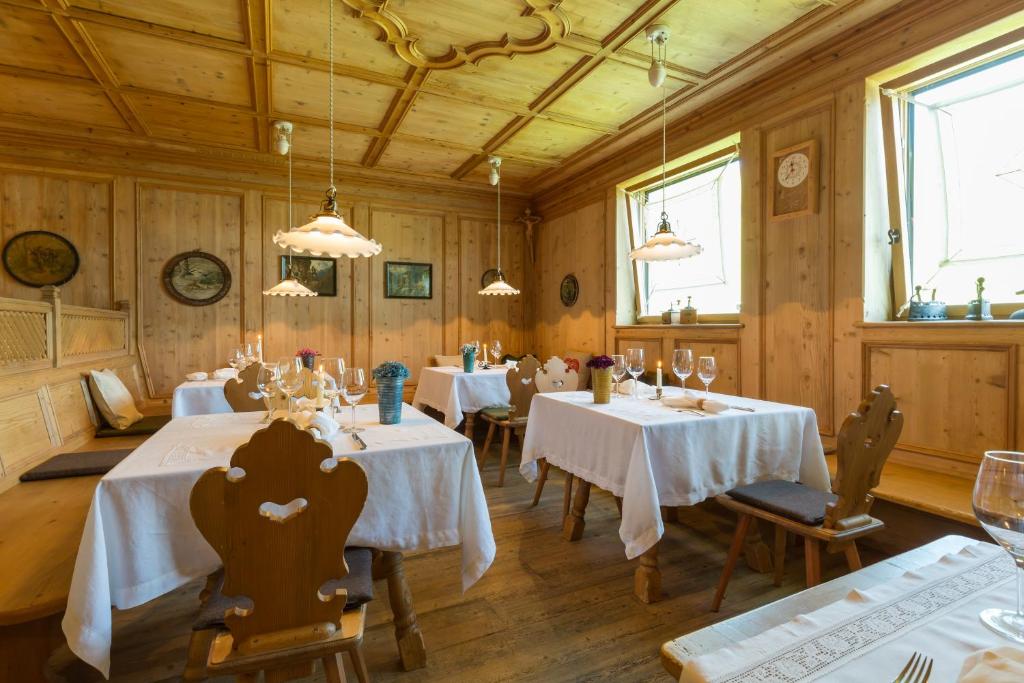 Klasiska koka interjera restorāna telpa ar baltām galda drānām, elegantiem galdiem un gaismas ķermeņiem. Logi ļauj ieplūst dabiskai gaismai, radot siltu un viesmīlīgu atmosfēru.