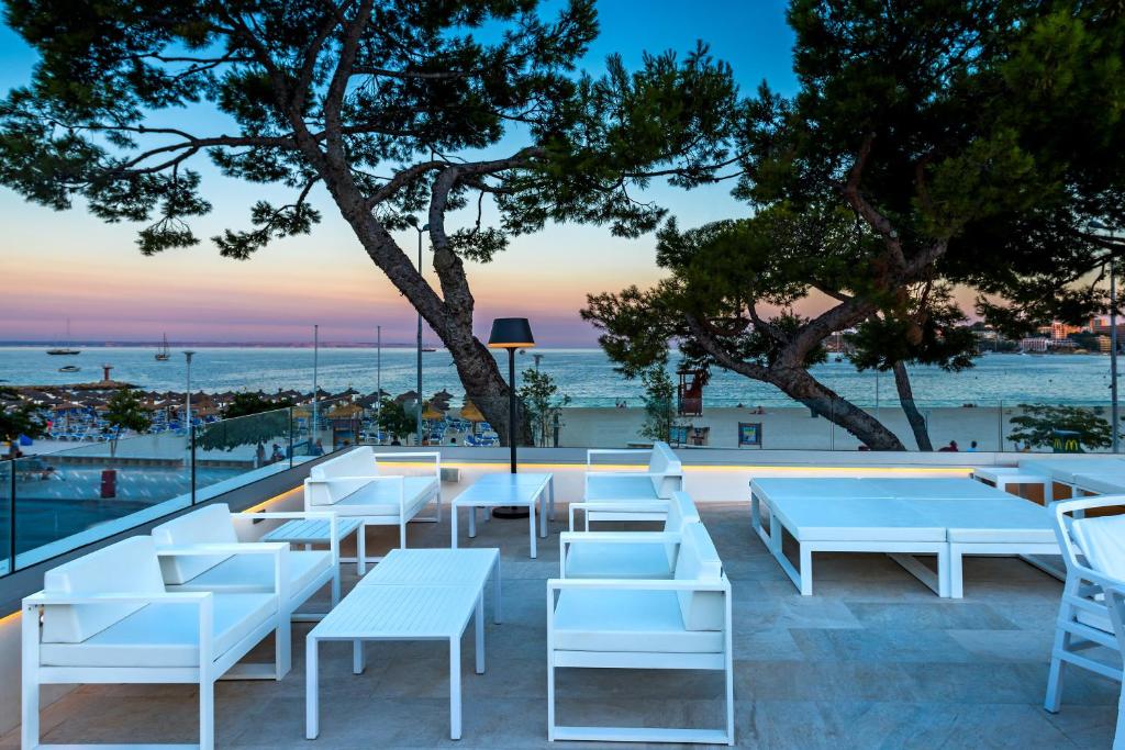 Moderns terases dizains ar baltām mēbelēm un skatu uz pludmali saulrieta gaismā. 