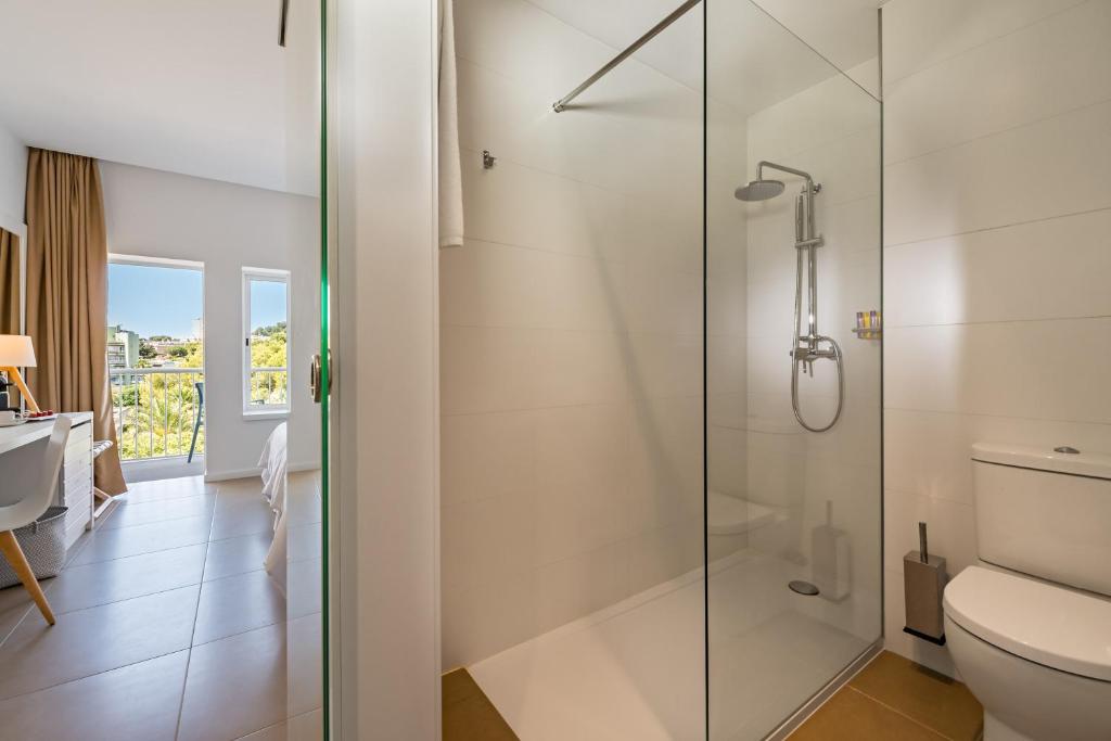 Mūsdienīgs vannas istabas interjers ar stikla dušas kabīni un tualeti, blakus guļamistaba ar logiem un darba stūri. Gaismas un telpas sajūta rada relaksējošu atmosfēru.