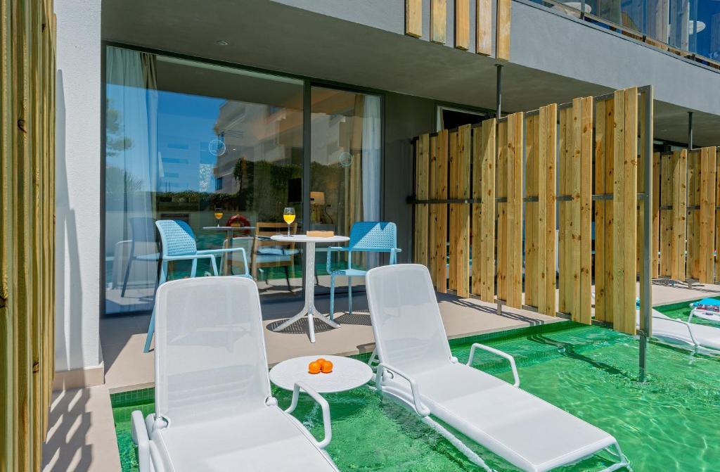 Mūsdienīga terase ar baseinu, kurā redzami saulessargi un dīvāni, ideāla atpūtai. Blakus ir galds ar krēsliem un dzērieniem, kas rada relaksējošu atmosfēru.