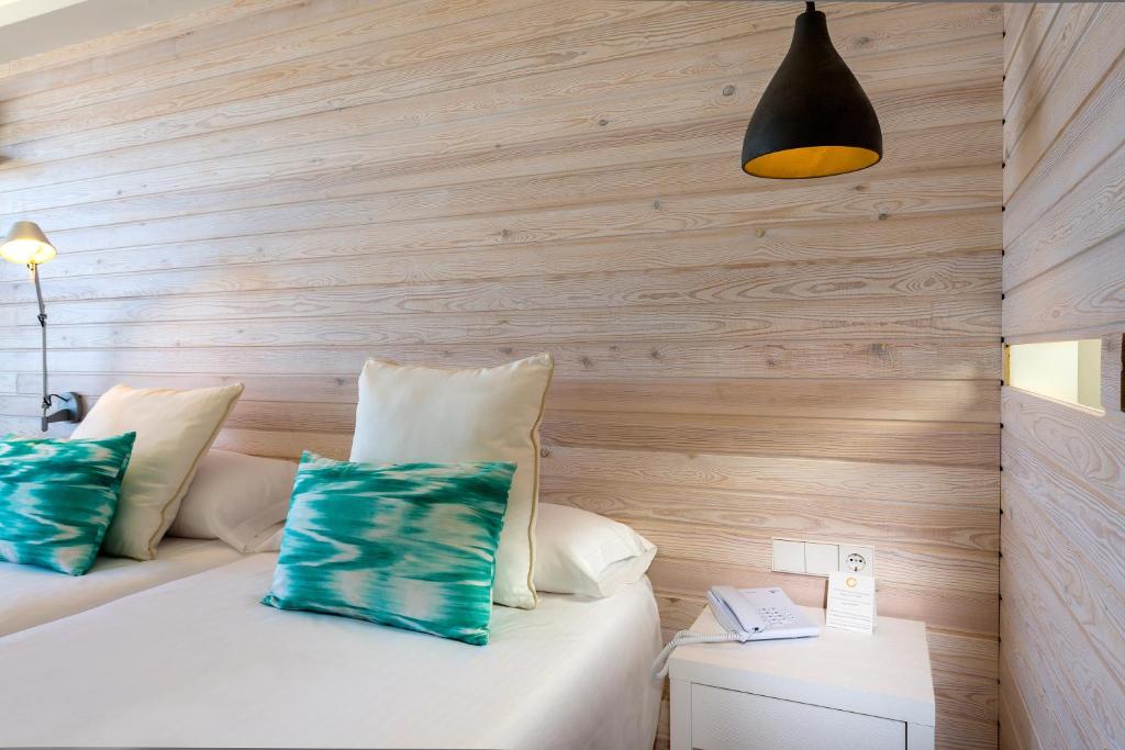 Mūsdienīgs guļamistabas interjers ar divām gultām, koka sienām un spilveniem ar zilu rakstu, papildināts ar ērtu galdiņu un lampu.