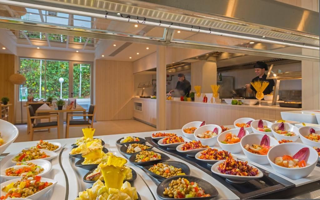 Svaigu salātu bufete modernā restorānā ar redzamām gatavošanas aktivitātēm fona. Dažādi krāsaini ēdieni no salātiem un garnējumiem.