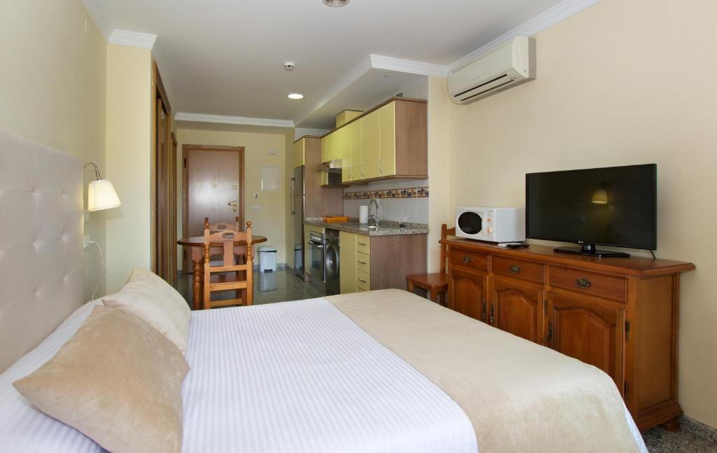 Mūsdienīgs viesnīcas numurs ar gultu, virtuves zonu un televizoru. Telpa ir gaiša un ērta, ar galdu un krēsliem.