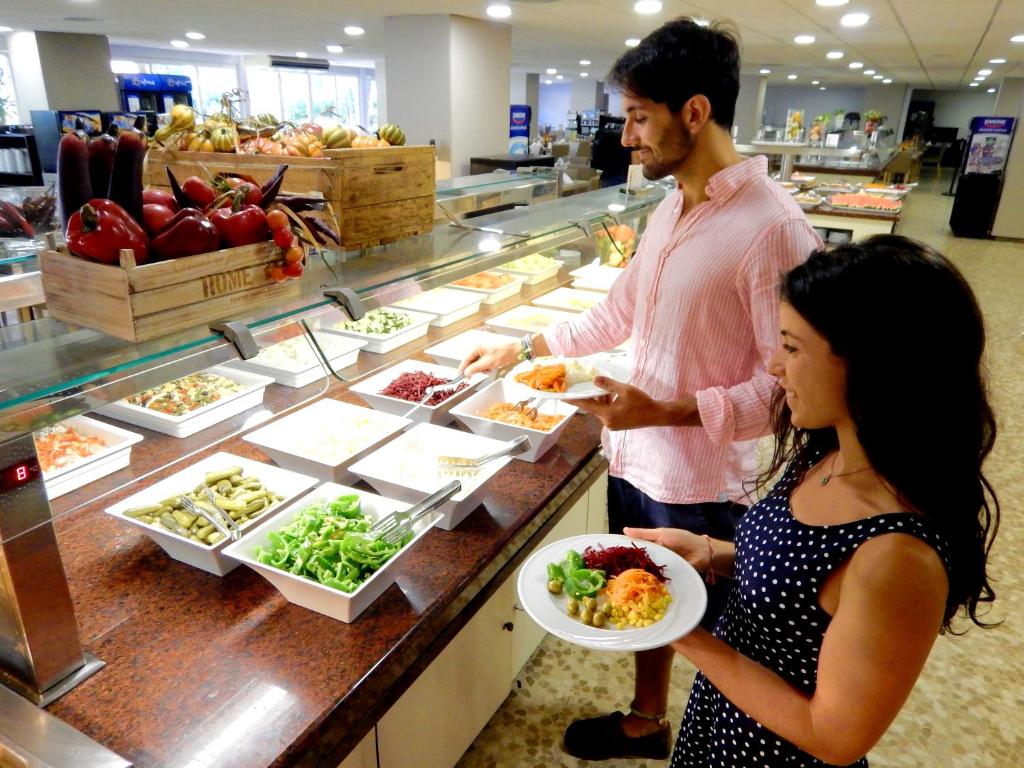 Pāris izvēlas veselīgas maltītes no bagātīgas bufetes, kurā redzami dažādi dārzeņu salāti un garnējumi.