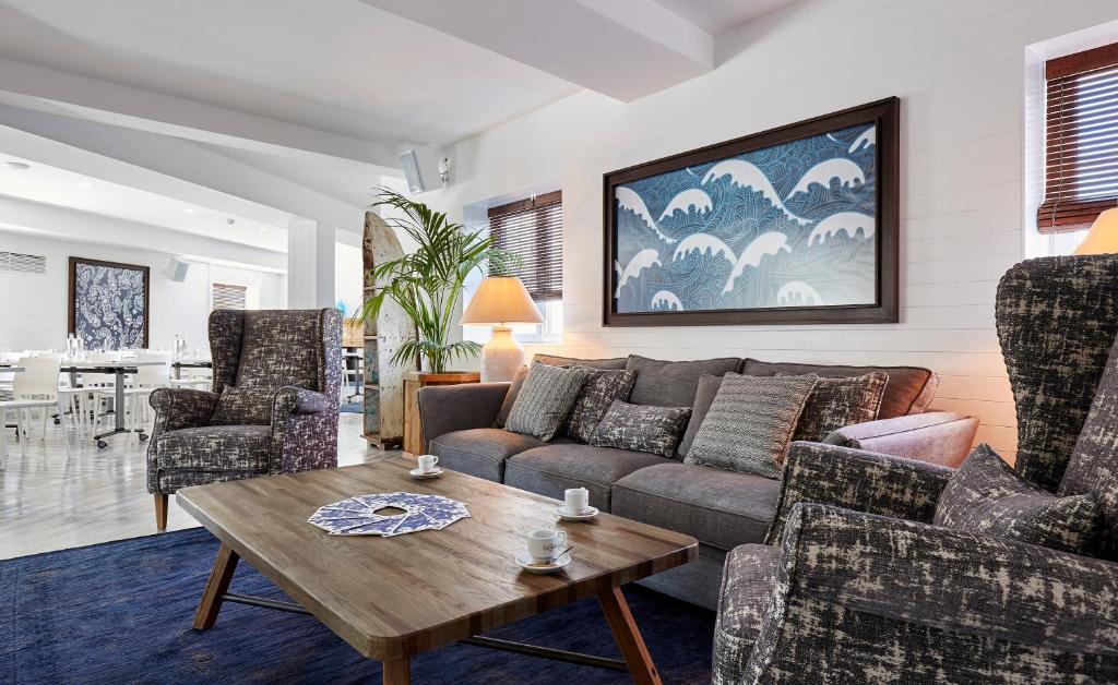 Mūsdienīga viesnīcas viesistaba ar ērtu dīvānu un krēsliem, koka galdu, dekoratīvām spilveniem un māksliniecisku gleznu uz sienas. Telpa ir gaiša un eleganta, radot relaksējošu atmosfēru.