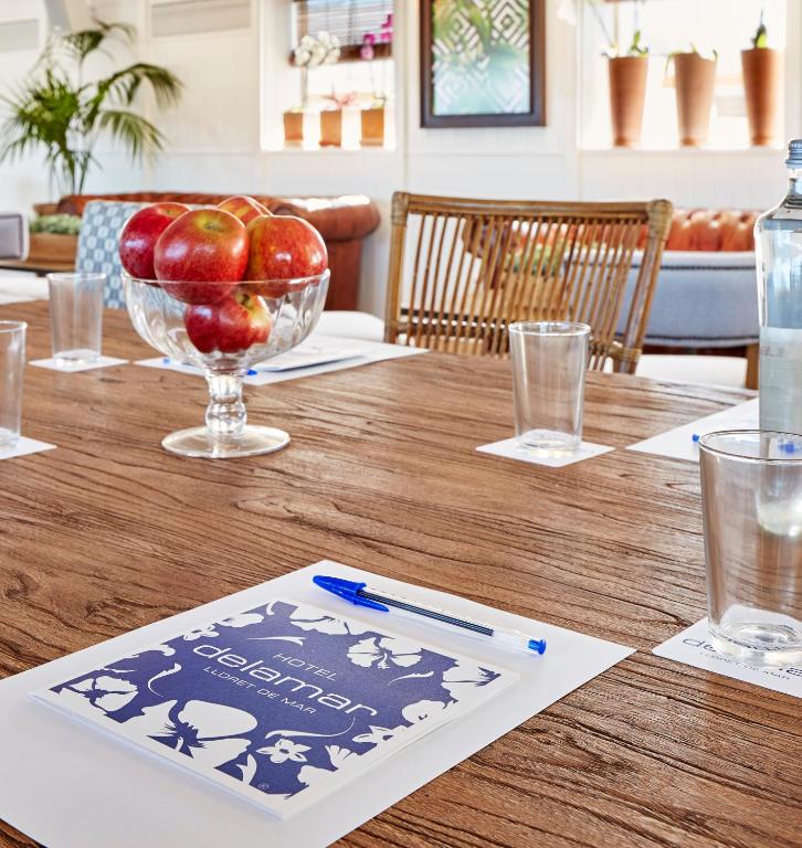 Konferences telpas galda skats ar sarkaniem āboliem stikla traukā, ūdens pudeli un piezīmju lapām ar viesnīcas "De La Mar" logo. Interjers ir gaišs un viesmīlīgs.