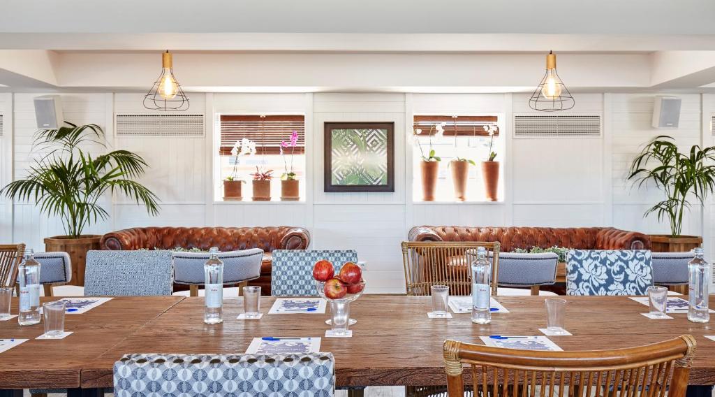 Mūsdienīgs un gaišs restorāna interjers ar koka galdu, krēsliem, zaļiem augiem un ērtām dīvāniem. Apgaismojums un dekorācijas rada viesmīlīgu atmosfēru.