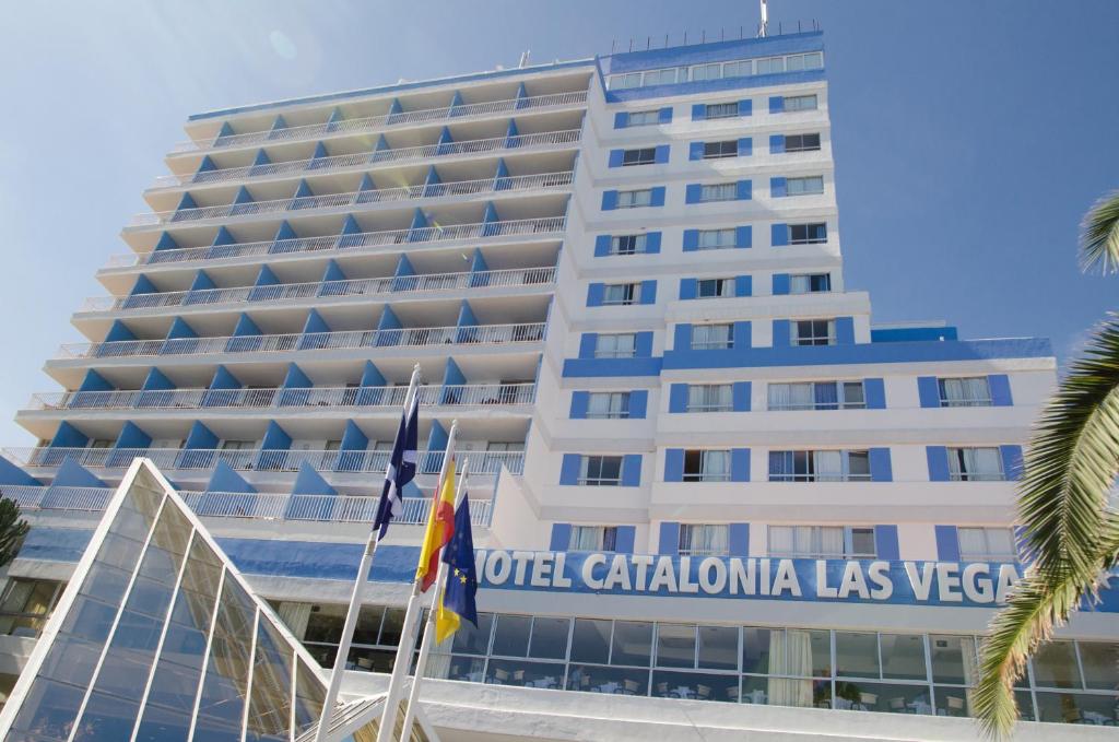 Mūsdienīgs viesnīcas ēkas dizains ar baltiem un ziliem akcentiem, kas atrodas saulainā vietā. Viesnīcas nosaukums "Hotel Catalonia Las Vegas" redzams uz fasādes.