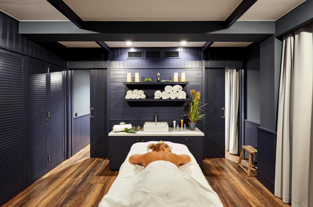 Mūsdienīgs spa telpa ar relaksējošu atmosfēru, kur masāžas galds ir centrālā uzmanības centrā, kam apkārt ir tīri dvieļi un augu akcenti.