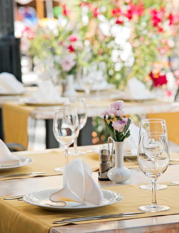 Elegants restorāna galds ar dzeltenu galdautu, salvetēm un glāzēm, papildināts ar ziedu kompozīciju. Ideāla atmosfēra romantiskai vai svinīgai maltītei.