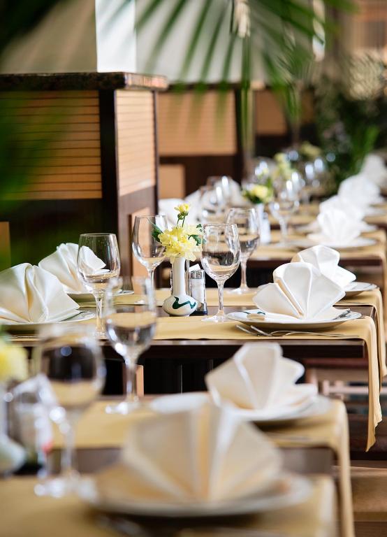 Elegantišķi klāta restorāna galda izkārtojums ar baltām salvetēm, glāzēm un ziediem. Gaisīga atmosfēra un rūpīgi sagatavotas vietas gaida viesus.