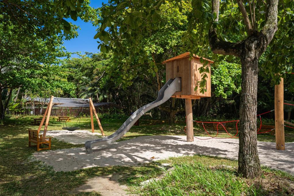 Kempinski Seychelles Resort bērnu rotaļu laukums ar koka namiņu un slidkalniņu zaļā dārzā.