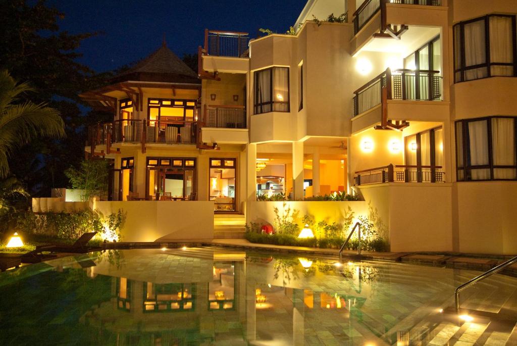 Eleganta viesnīca ar baseinu, kas apgaismota naktī, radot mierīgu atmosfēru. Viesnīcas arhitektūra apvieno modernus un tradicionālus elementus.